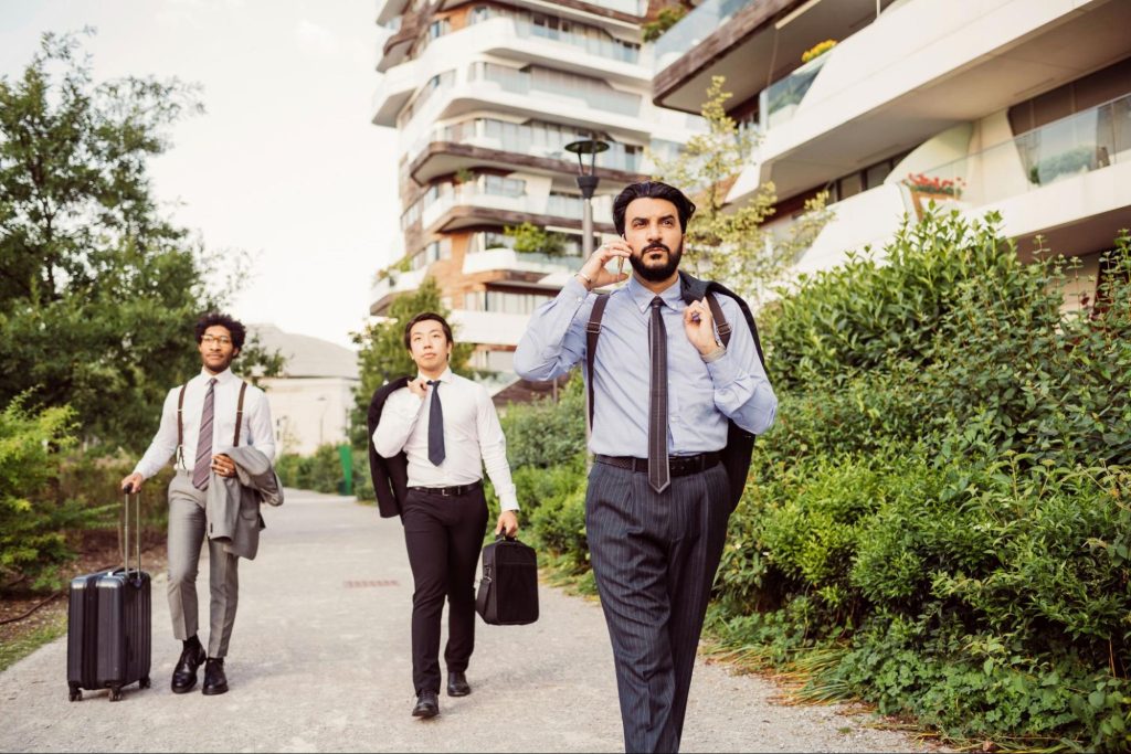 Young professionals walking near modern apartment buildings in Dallas with luggage and briefcases.